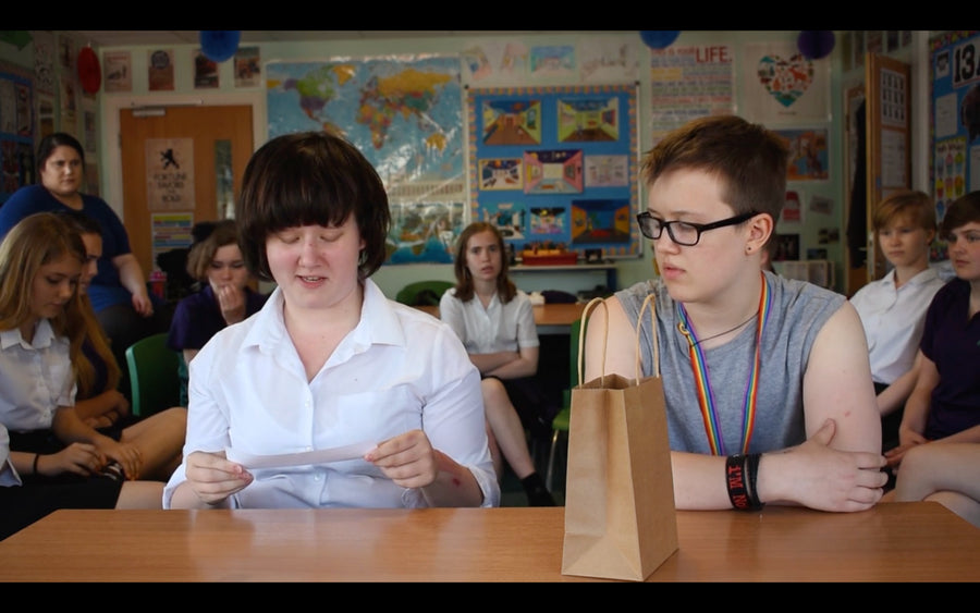 Students seated at a classroom table during a group activity, with a paper bag placed in the center