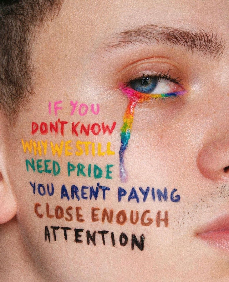 Close-up of a person’s face featuring a rainbow-colored tear and handwritten text painted on the skin