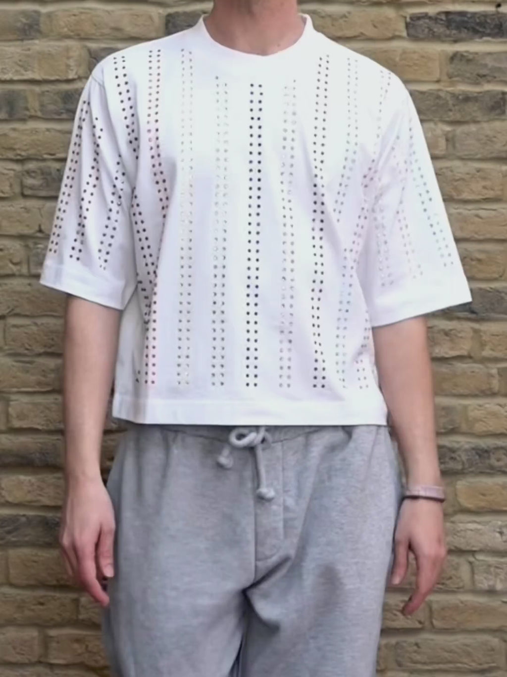 Model wearing white Proud T-shirt with rainbow crystal , pride inspired, lines against a brick wall