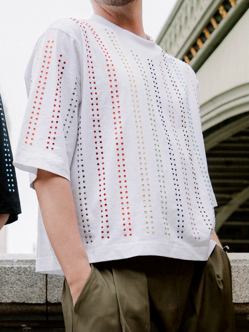 Model wearing white Proud T-shirt with vertical rainbow crystal lines , pride inspired, outdoors