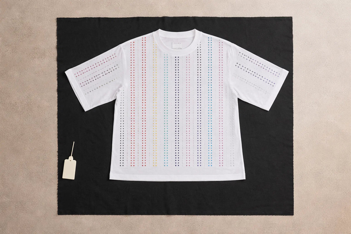 White Haus of Mx. Proud T-shirt laid flat with vertical rainbow rhinestone stripes,  pride inspired, on a contrasting background