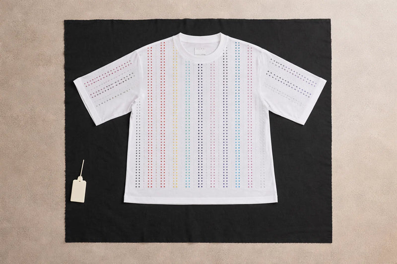 White Haus of Mx. Proud T-shirt laid flat with vertical rainbow rhinestone stripes,  pride inspired, on a contrasting background
