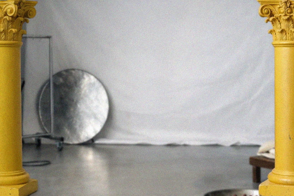 Yellow corintian style columns with a gray backdrop and round metallic object on wheels.